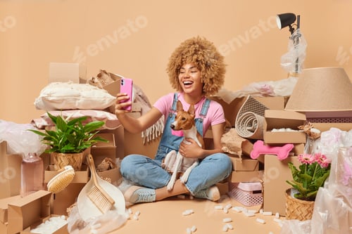 Preview: Positive carefree woman takes selfie via smartphone poses with pedigree dog in own apartment surroun