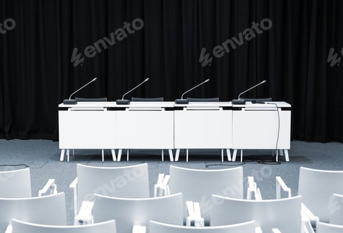 Preview: Monochrome picture of empty press conference room with seats, stand table and microphones