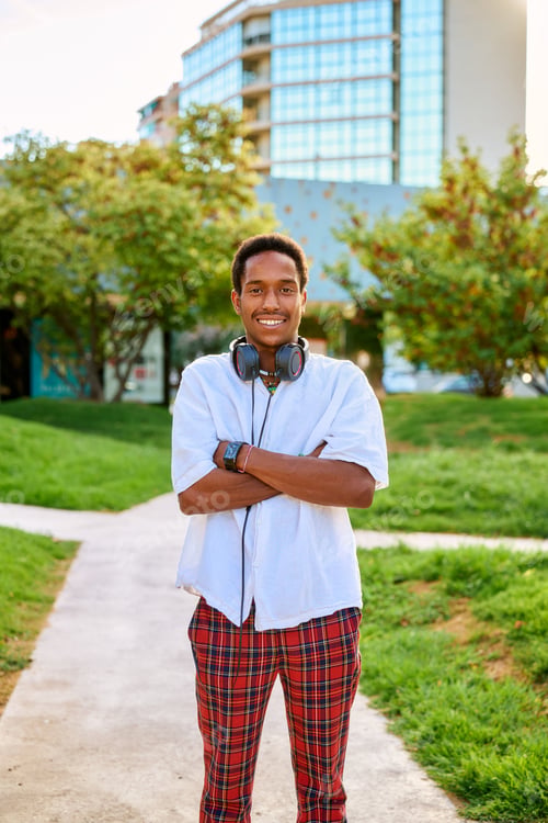 Preview: A young man smiles proudly with his arms crossed, wearing headphones, in a lively outdoor area