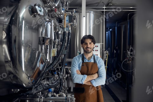 Preview: A man in an apron stands confidently in a factory, arms crossed