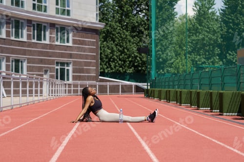Preview: African American woman takes break from intensive training resting on running track of sports ground