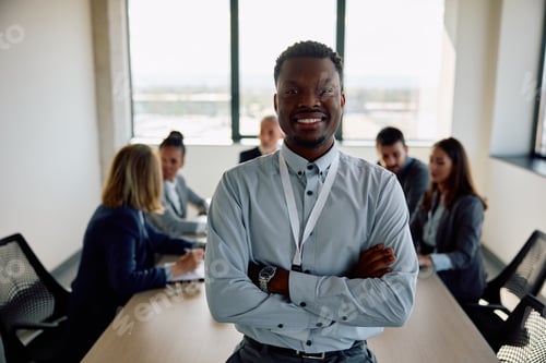 Preview: Happy black CEO with arms crossed in meeting room looking at camera.