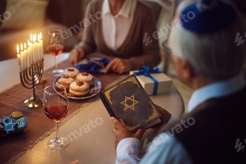 Preview: Close up of senior couple reading Hebrew bible during Hanukkah celebration at home.