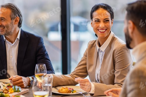 Preview: Portrait of businesswoman sitting with coworkers in restaurant during business lunch.