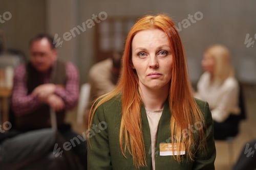 Preview: Serious middle aged woman in casualwear looking at you while sitting against patients and counselor