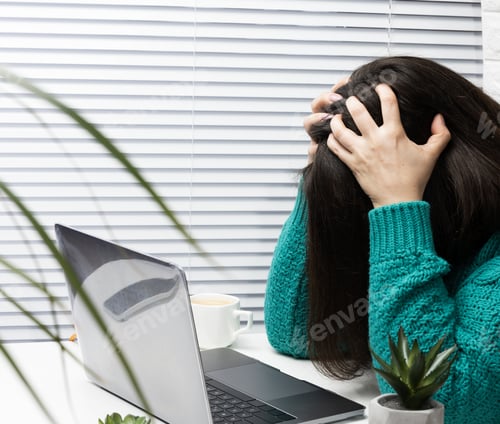 Preview: woman in a sweater sits at the table with her head clasped in her hands, stress and headache
