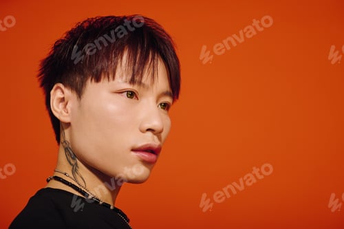 Preview: Stylish young asian man poses confidently against a vibrant orange backdrop in creative portraiture