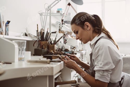 Preview: Focused on a process. Portrait of young female jeweler focused on creating a silver ring at her