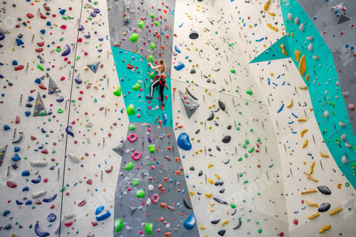 Preview: Rock climber young woman hanging on colored hooks on climbing artificial wall indoors of sport