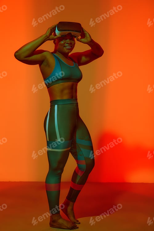 Preview: Modern african black woman with short hiar in sport top wearing glasses of virtual reality on yellow