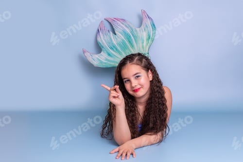 Preview: A smiling child girl in a mermaid costume lie on a blue background