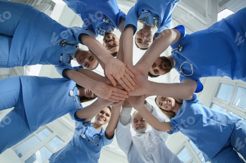 Preview: Doctor and interns stacking hands together indoors, bottom view