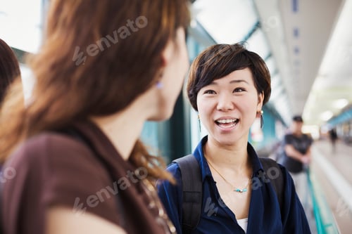 Preview: Two women standing indoors, looking at each other, smiling.