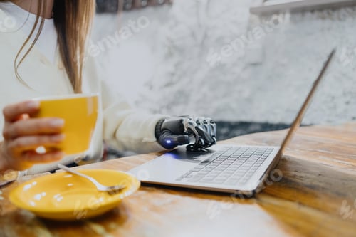 Preview: woman with a bionic prosthetic arm is working on a laptop and drinking coffee in a coffee shop