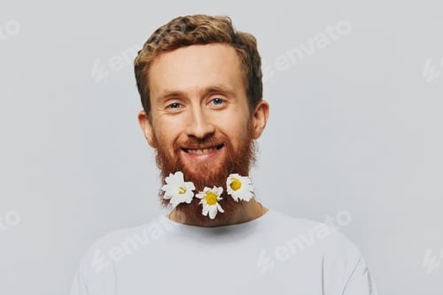 Preview: Portrait of a funny man in a white T-shirt with flowers daisies in his beard on a white isolated