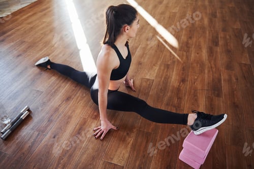Preview: Beautiful sporty woman in sportswear doing stretching by using equipment on the floor