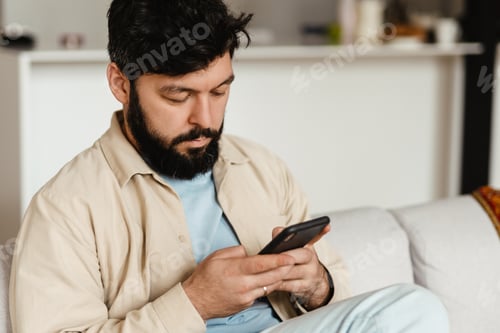 Preview: White bearded man using cellphone while sitting on couch at home