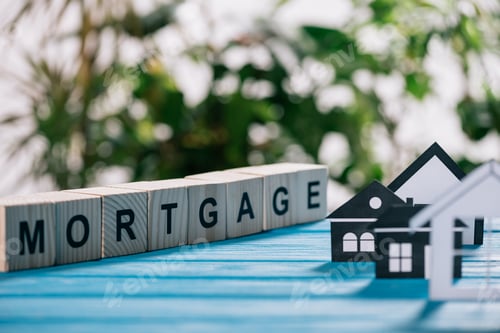 Preview: selective focus of paper houses near cubes with letters on blue wooden desk, mortgage concept