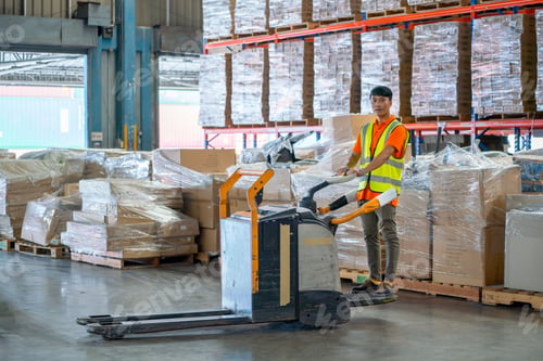Preview: Asian warehouse worker stand and drive folklift in front of stack of product carton in workplace