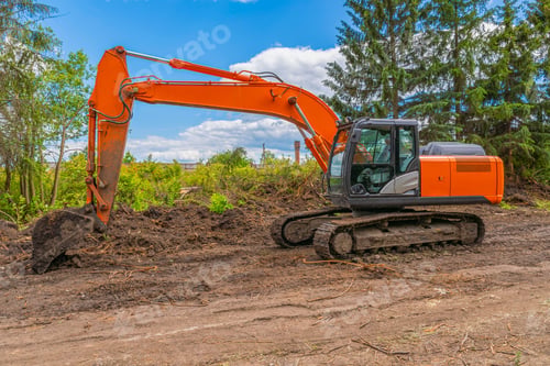 Preview: Orange new crawler excavator stands against backdrop of green trees and blue cloudy sky.