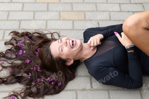 Preview: top view of a woman with purple lilacs flowers in her hair laughing on the pavement