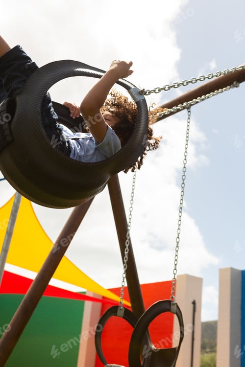 Preview: Mixed-race schoolgirl playing in a swing swing in the school playground on a sunny day
