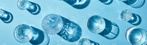 Preview: top view of transparent glasses with clear water on blue background, panoramic shot