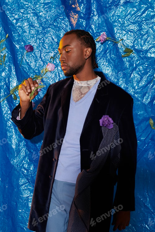 Preview: Young man explores beauty with flowers against a vibrant blue backdrop