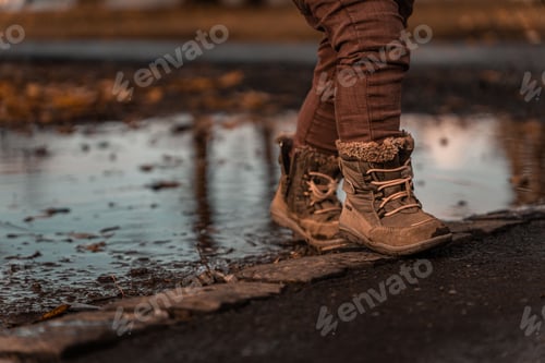 Preview: Child standing on the pavement with a puddle in the background on a cold autumn day