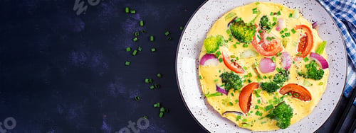 Preview: Omelette with broccoli, tomatoes and red onions on dark table.