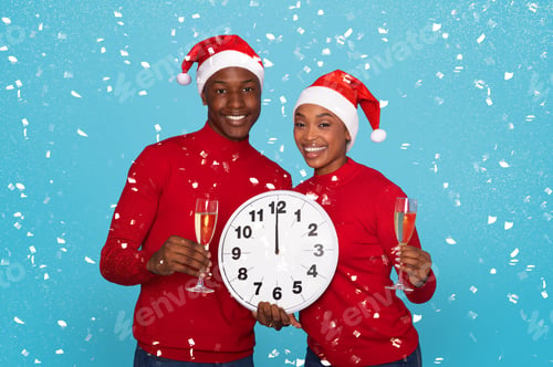 Preview: Couple In Santa Hats Holding Champagne Glasses And Clock, Studio