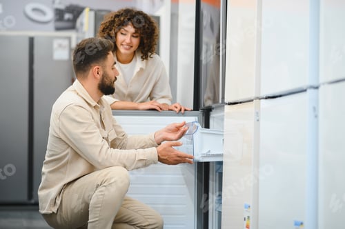 Preview: Couple choosing refrigerator in electronics store examining freezer compartment
