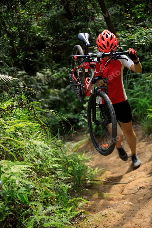 Preview: Woman cyclist carry a mountain bike walking on tropical forest trail