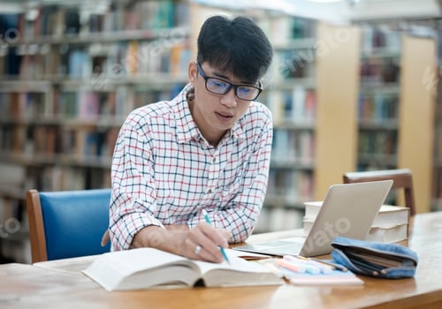 Preview: Young Asian male sitting inside a library alone doing research.
