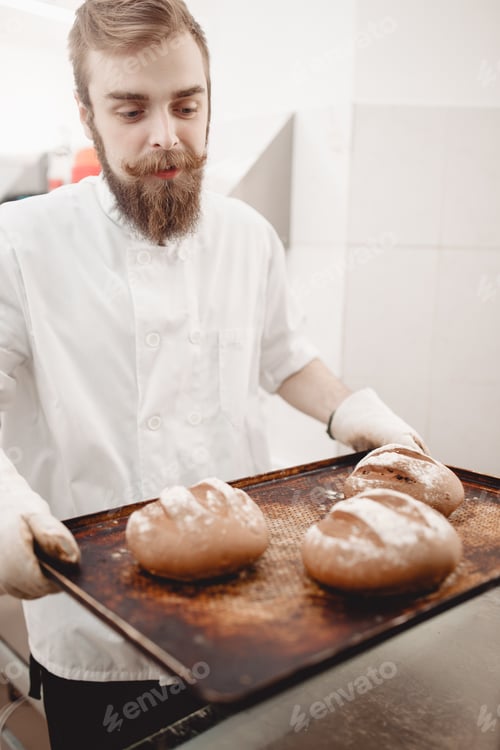 Preview: Charismatic baker holds the baking tray with newly-baked bread in the bakery