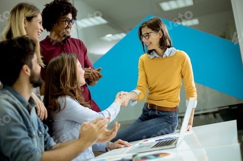Preview: Group of young coworkers interacting around a table and handshaking in the office