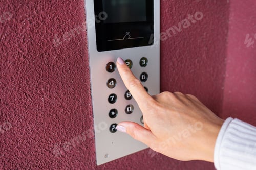 Preview: A young woman dials the apartment code on the panel of an electronic intercom.