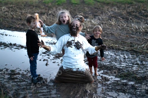 Preview: Happy woman and three children having fun on muddy field