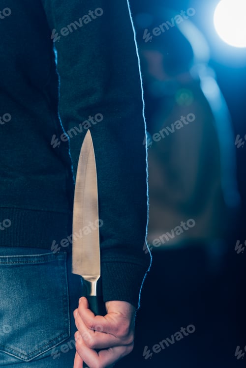 Preview: cropped view of murderer hiding knife behind back on black