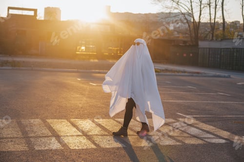 Preview: Girl in white bedsheet and sunglasses dressed as a ghost on Halloween walks down the street