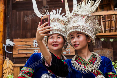 Preview: China, Guizhou, two Miao women wearing traditional dresses and headdresses taking a selfie with smar
