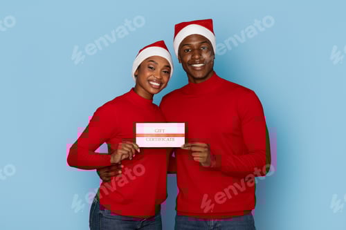 Preview: Cheerful couple in red sweaters holding gift certificate against blue backdrop