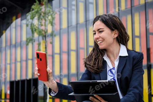 Preview: Entrepreneur working with multiple devices sitting in a bench in a trendy park. First plane.