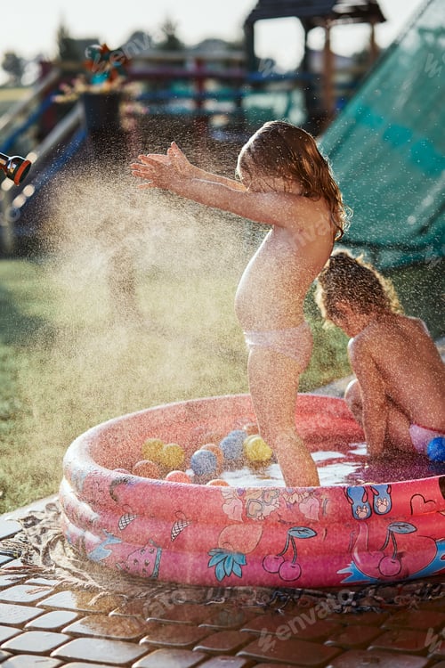 Preview: Little cute adorable kids enjoying a cool water sprayed by their father during hot summer day in