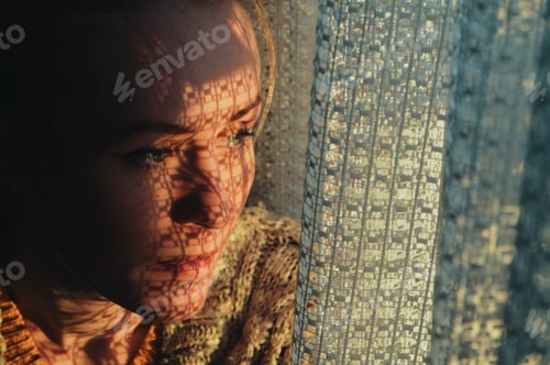 Preview: portrait of a woman standing next to a window, sunset through curtain cast a shadow on her face