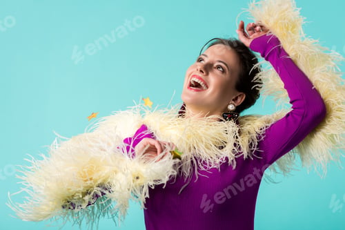 Preview: happy party girl in purple dress with feathers under falling confetti isolated on turquoise