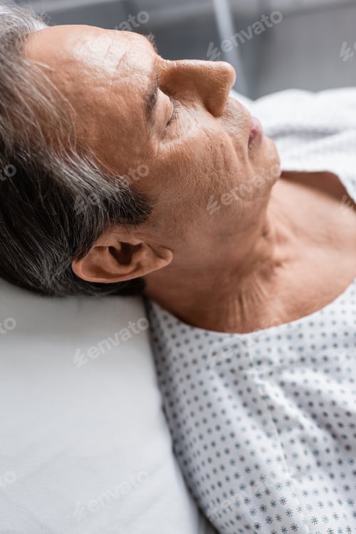 Preview: Elderly patient lying on blurred bed in hospital ward