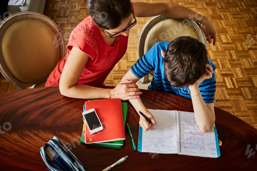 Preview: High angle view of mother at dining table helping son with homework