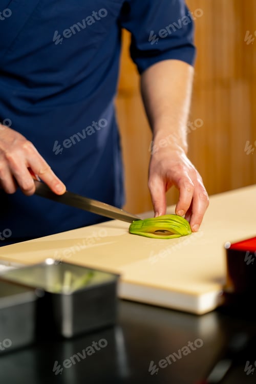 Preview: close up in a Japanese restaurant a chef in a blue uniform cuts avocado sushi into slices on a