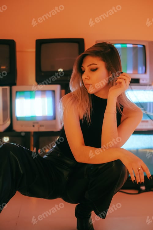 Preview: Portrait of young attractive caucasian woman in stylish outfit posing near stand with retro tvs.
